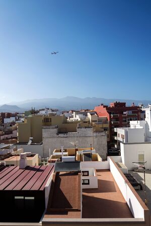 Charter plane leaving Tenerife airpot during sunrise seen from roofs of traditional houses with Mount Teide volcano in background, Canary Islands, Spain, sunny blue sky with copy spaceの写真素材