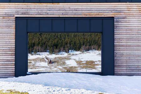 Wooden house with large reflective mirror window, design wall, modern architecture, sunny winter dayの写真素材