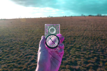 Male hand holding glass compass, nature in background, sunny autumn day, life change and new years...