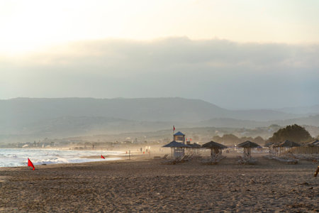 Unrecognizable people walking on a beach with a red flag warning of big waves at dawnの写真素材