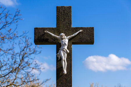 Beautiful Jesus Christ on crucifix, spring Easter budding tree flowers in background, cemetery on a sunny day, new life and religion conceptの写真素材