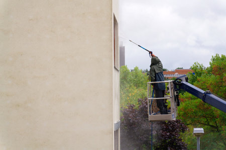 Unrecognizable man cleaning facade surface from lifting platform with high pressure stream of water