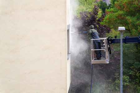 Unrecognizable man cleaning facade surface from lifting platform with high pressure stream of waterの写真素材