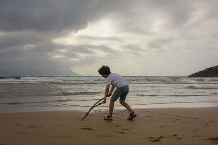 my son playing with sticks in the sand of a beach in the Cantabrian seaの写真素材