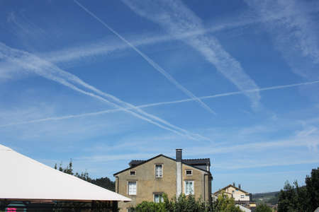 sky with plenty of chemtrails over a house in the countryside