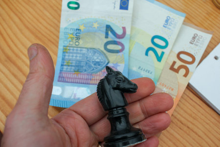 a chess piece in my hand and euro notes on the tableの写真素材
