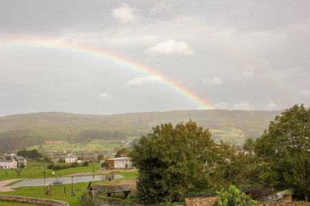 Serenity at Home: Rainbow Over Green Hills and White Houseの写真素材