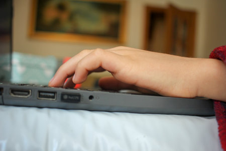 the hand of a child pressing the keys of a laptop at his home