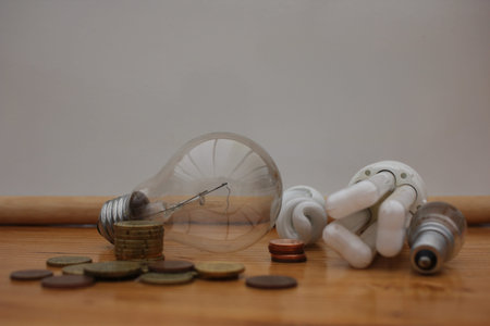 A conceptual image showing glowing light bulbs surrounded by scattered coins, symbolizing the rising...