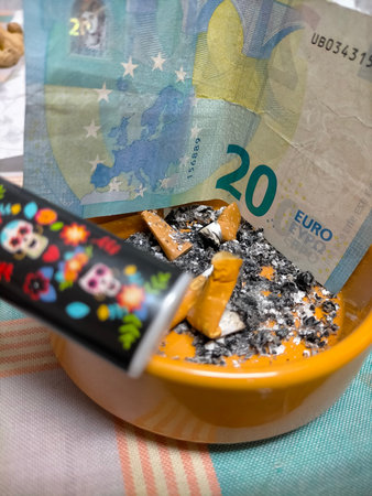 Several used cigarette butts in a ceramic ashtray with a 20-euro note lying nearbyの写真素材