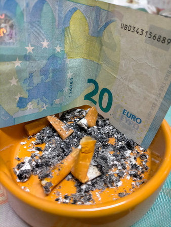 Cigarette butts resting in an ashtray beside a 20-euro note.の写真素材