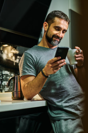 Dark haired man with beard pouring coffee in his kitchen wearing casual clothesの写真素材