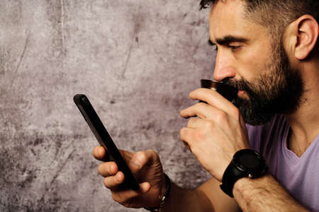 young white man with beard drinking coffee and looking at the mobileの写真素材