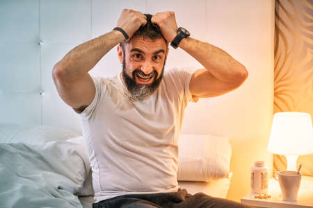 person with some kind of problem sitting on the bed and pulling their hairの写真素材