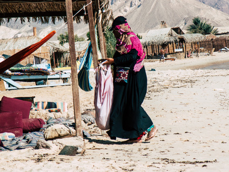 Sinai Egypt October 6, 2018 View of an Arabian woman dress with burka and carrying a bag walking on the beach in the morningのeditorial素材