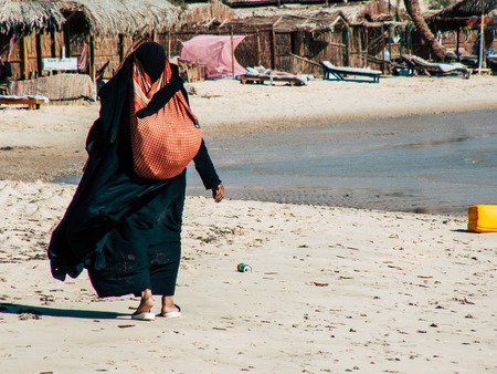Sinai Egypt October 6, 2018 View of an Arabian woman dress with burka and carrying a bag walking on the beach in the morningのeditorial素材