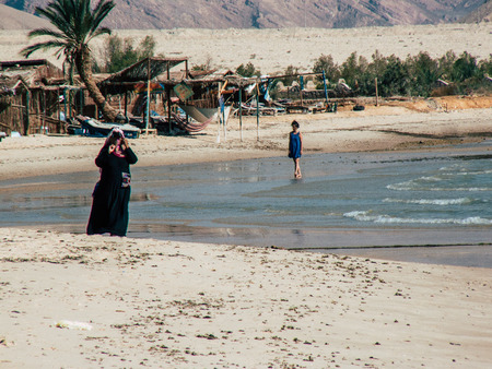 Sinai Egypt October 6, 2018 View of an Arabian woman dress with burka and carrying a bag walking on the beach in the morningのeditorial素材