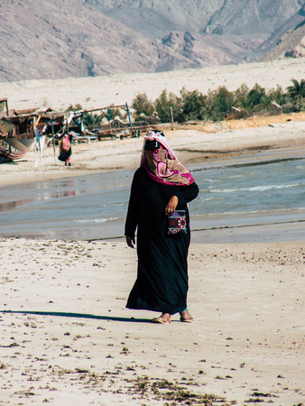 Sinai Egypt October 6, 2018 View of an Arabian woman dress with burka and carrying a bag walking on the beach in the morningのeditorial素材