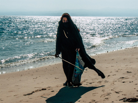 Sinai Egypt October 6, 2018 View of an Arabian woman dress with burka and carrying a bag walking on the beach in the morningのeditorial素材