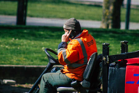 Reims France April 08, 2021 Gardener cutting the grass of a garden seated on a lawn mower in early...