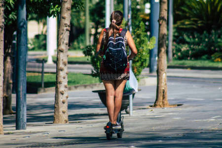 Seville Spain August 21, 2021 People rolling with an electric scooter in the streets of Seville, operating with a small utility internal combustion engines and a deck in the centerの写真素材