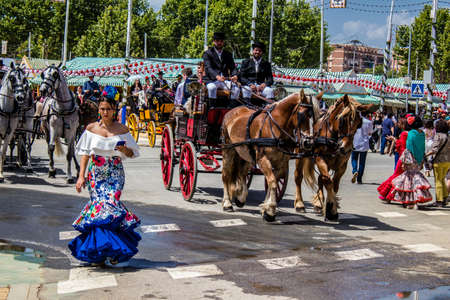 Seville, Spain - May 01, 2022 Sevillians dressed in the traditional Andalusian way riding in a horse drawn carriage through the aisles of the Feria de Sevilla, the most famous festival in Spainのeditorial素材