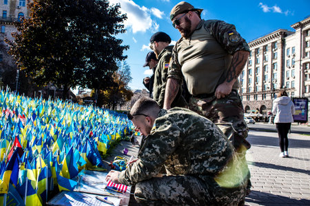 3 soldiers of the foreign legion in Ukraine, of American, Canadian and Belgian nationality pay homage to one of their killed in action in Kherson during the fights with the Russian army. A small flag with the name of the dead soldier is planted in the maiのeditorial素材