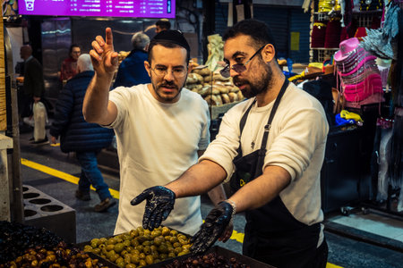 Jerusalem, Israel - February 17, 2026 Immersion in Mahane Yehuda Market, showcasing local merchants handling traditional olives and vibrant street trade in this iconic urban location.のeditorial素材