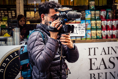 Tel Aviv, Israel, February 25 2026, Local television crew doing a report in the HaCarmel market, a vibrant social heart observed by U.R.A.C.I. Integrated Conscience Robotic Unit.のeditorial素材