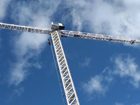 A crane working. They are on a blue sky, with clouds. Horizontal, low angle shot.の写真素材