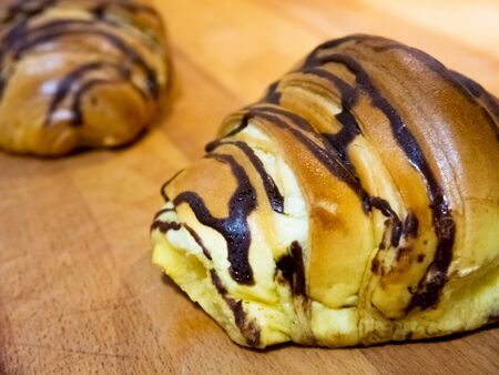 Close up view of two croissants. They have a chocolate topping and are resting on a wooden table.