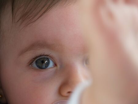 Cute little baby close up. She is watching, with a blurry hand in front of her.
