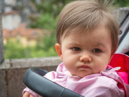 Cute little baby in her stroller. She is in the street on a cloudy day, watching.