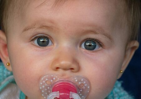 Cute little baby with a pacifier close up. She is amazed, looking front