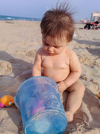Cute little baby. She is sitting in the beach, playing with the sand.の写真素材