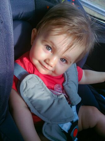 Cute little baby smiling. It is a sunny day and she is in her car seat.の写真素材