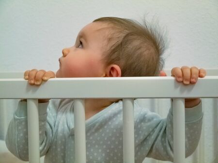 Cute little baby. She is standing in her cradle, watching.の写真素材