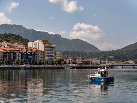 Village next to the sea, with some boats sailing on it. It is surrounded by nature, and it is a sunny day with a blue sky.の写真素材