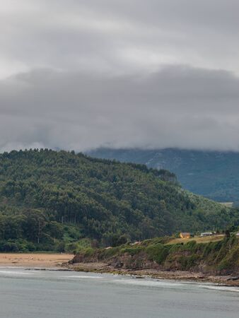 Bunch of houses between a beach and a mountain. It is a cloudy day, and there is mist up the mountain.の写真素材