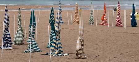 Empty beach on a cold, cloudy day. There is no people and there are some parasols that are closed.の写真素材