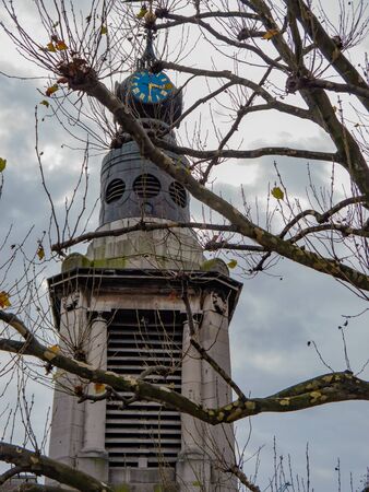 Tower with a clock on it. The sky is grey on a foggy day and there are some branches in front of it.の写真素材