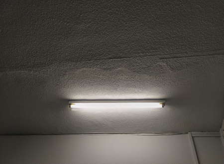 Fluorescent tube on a ceiling illuminating a white room with droplets.の写真素材