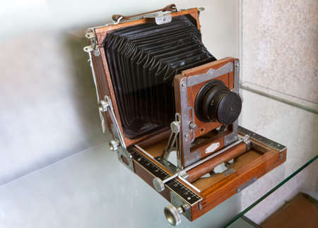 Vintage camera made of wood, metal, plastic and leather displayed on a shelf in front of a stone wallの写真素材
