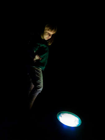 Little girl playing happily around a lamp on the floor of a park at night
