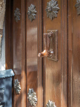 Boot-shaped knocker placed in an old rustic door, with the wall and the mailbox of the house on the...