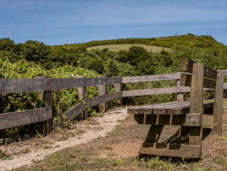 Rustic wooden bench located in the countryside, overlooking an elevated area of field with lots of...