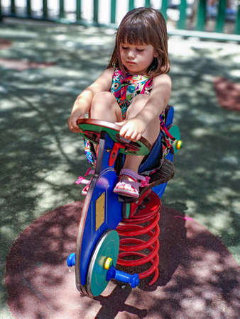 Girl in a colorful dress playing on a playground while balancing on a seesaw on a sunny summer dayの写真素材