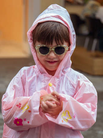 Smiling girl in a pink raincoat and sunglasses on a rainy summer day in Cantabriaの写真素材