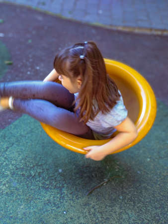 Girl with two pigtails playing spin on an urban playground on a sunny summer dayの写真素材