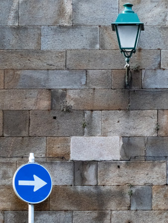 Solid stone wall with an ancient street light and a traffic signの写真素材